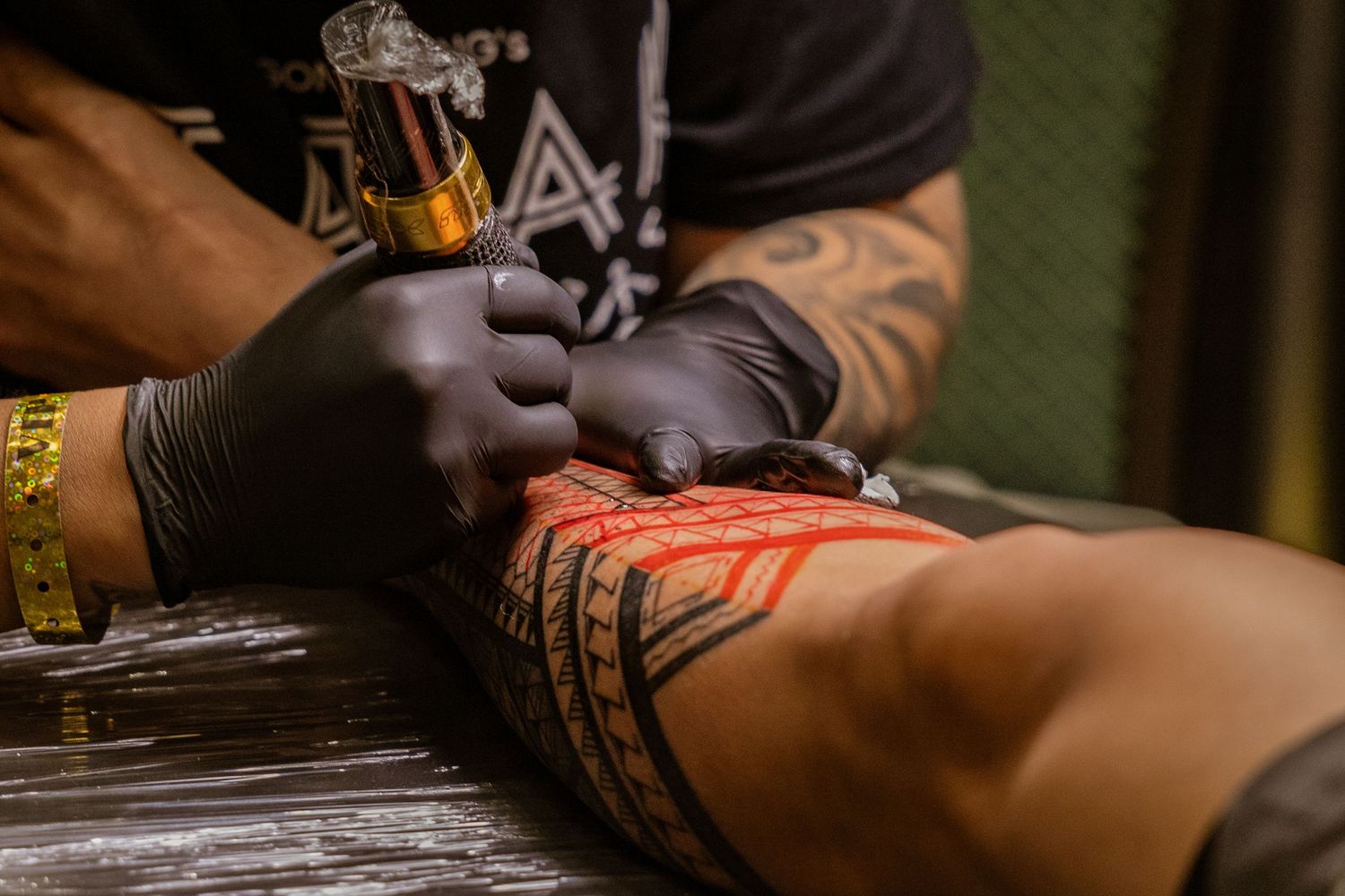 Close-up of tattoo machine creating red and black tribal design on skin.