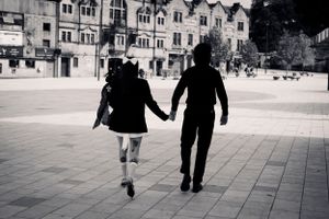 Black and white photo of a couple holding hands, timeless romance and city life captured in motion.