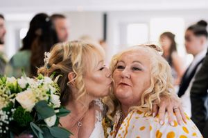 Joyful wedding moment—bride shares a loving kiss with a guest, surrounded by smiles and celebration. Perfect for capturing candid emotions.