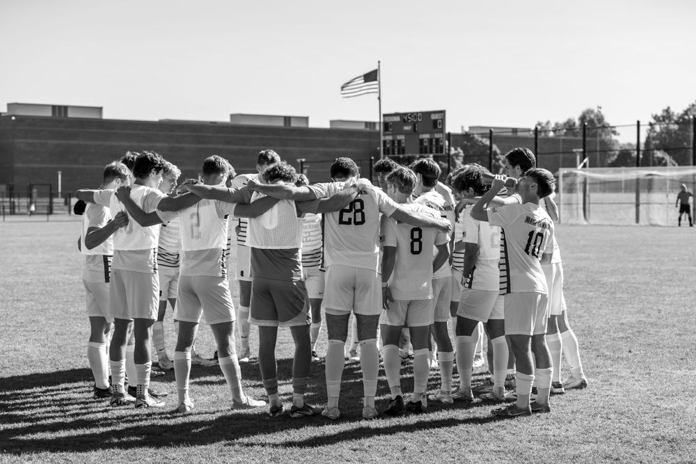 Soccer team huddles together on field in black and white photograph.