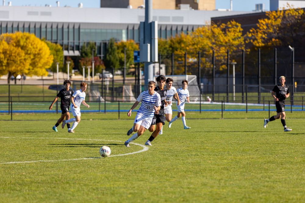 Soccer players chase ball during competitive match on sunny grass field.