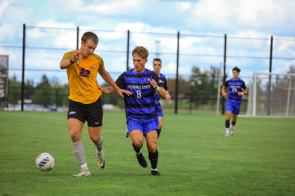 Soccer players in yellow and blue uniforms battle for possession during match.