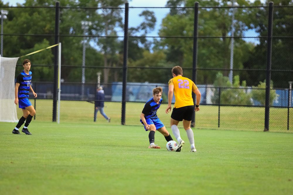 Soccer players in blue and yellow jerseys compete for ball on grass field.