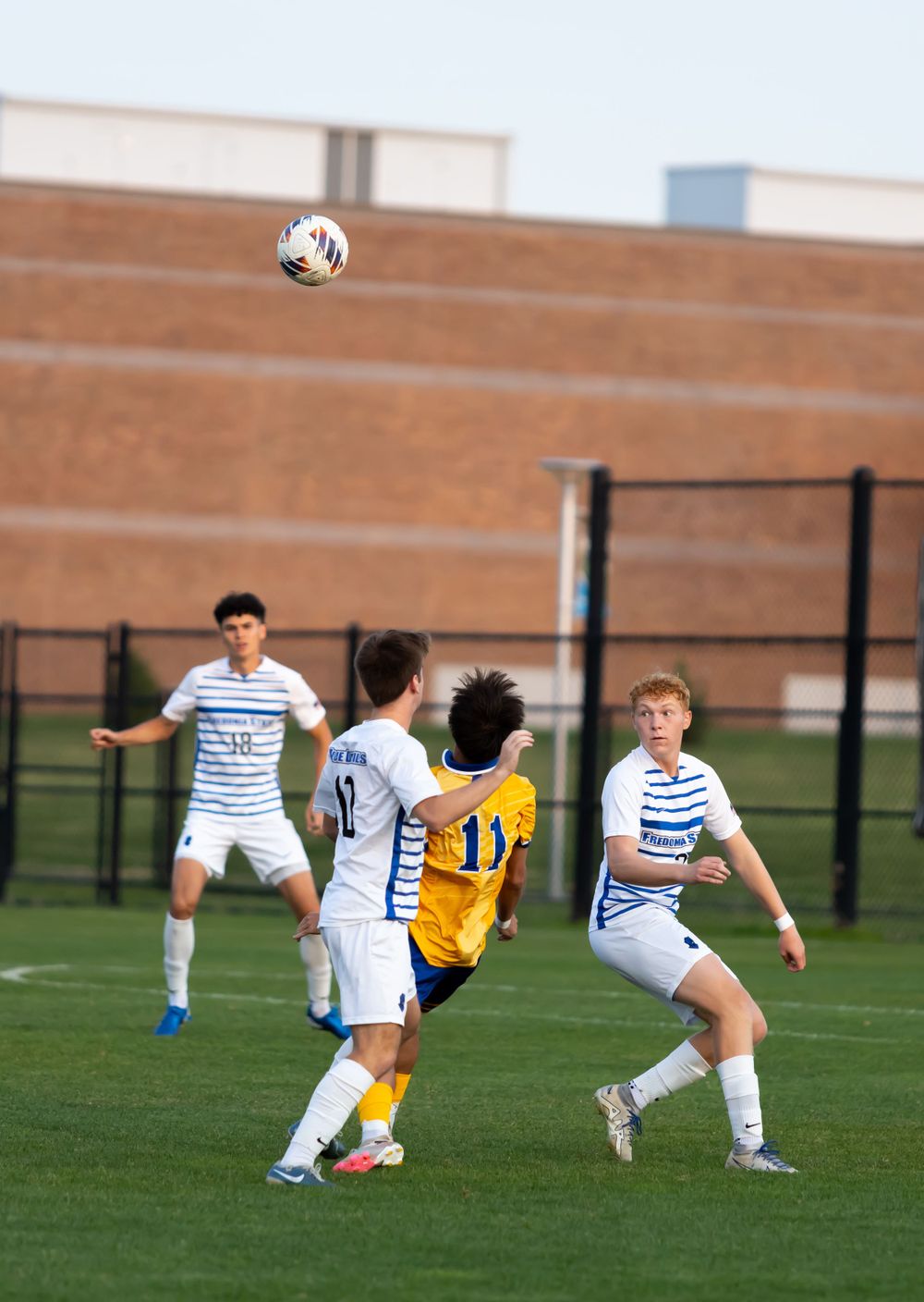 Soccer players jump for header during competitive match on school field.