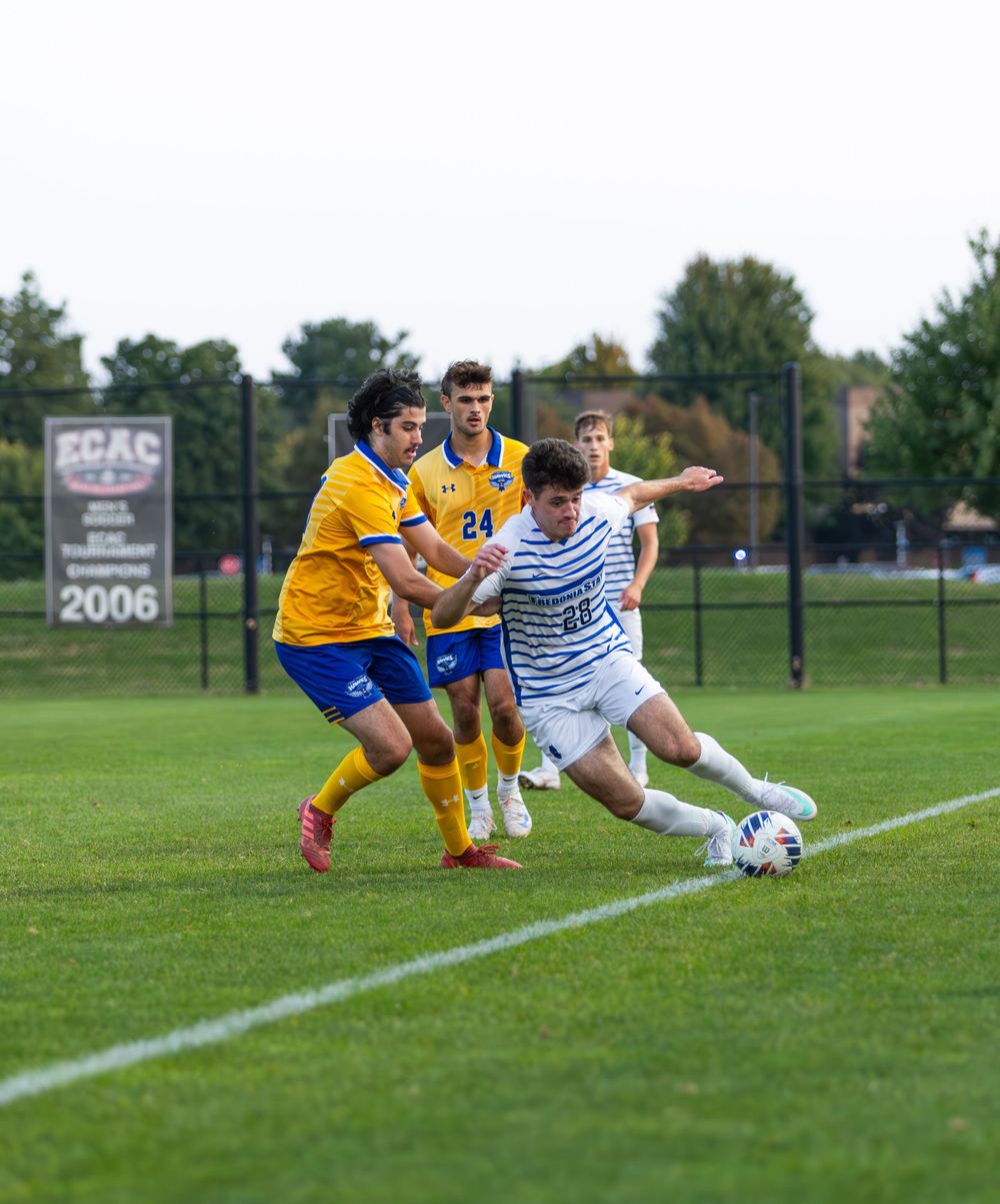 Soccer players in yellow and white uniforms compete for the ball on a grass field during a match.