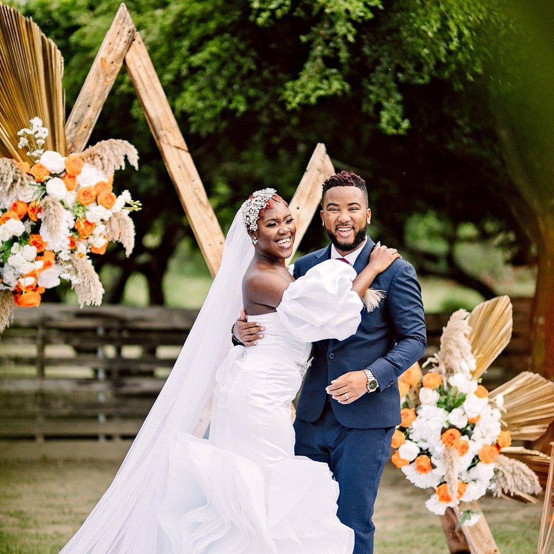 Elegant wedding ceremony features a triangular arch decorated with orange and white floral arrangements in an outdoor setting.