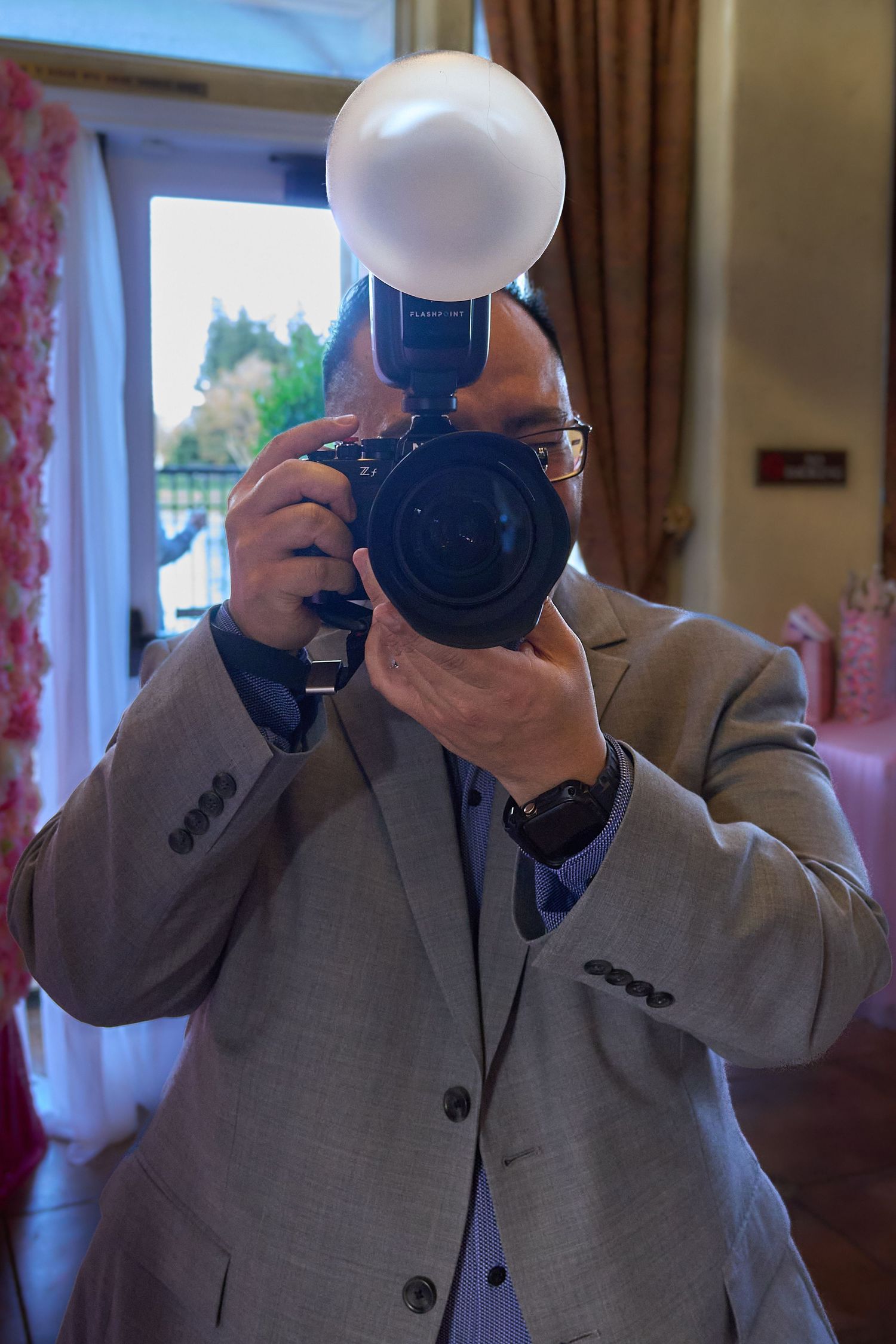 A photographer in a gray suit takes a series of self-portraits with a camera and flash in an indoor setting.