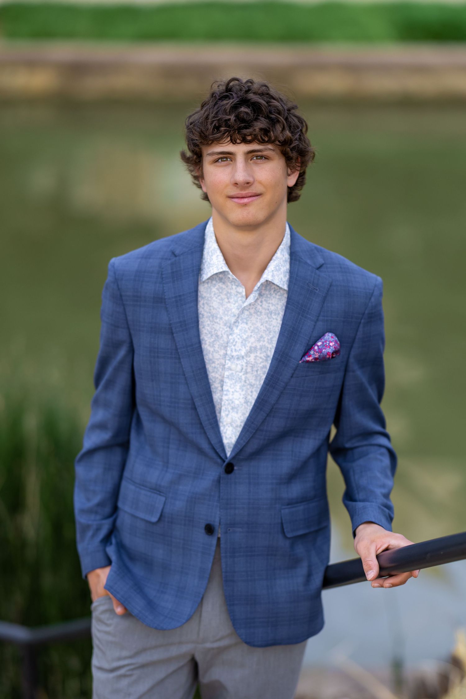 Professional portrait of someone wearing a blue plaid blazer and white shirt near a waterfront setting.