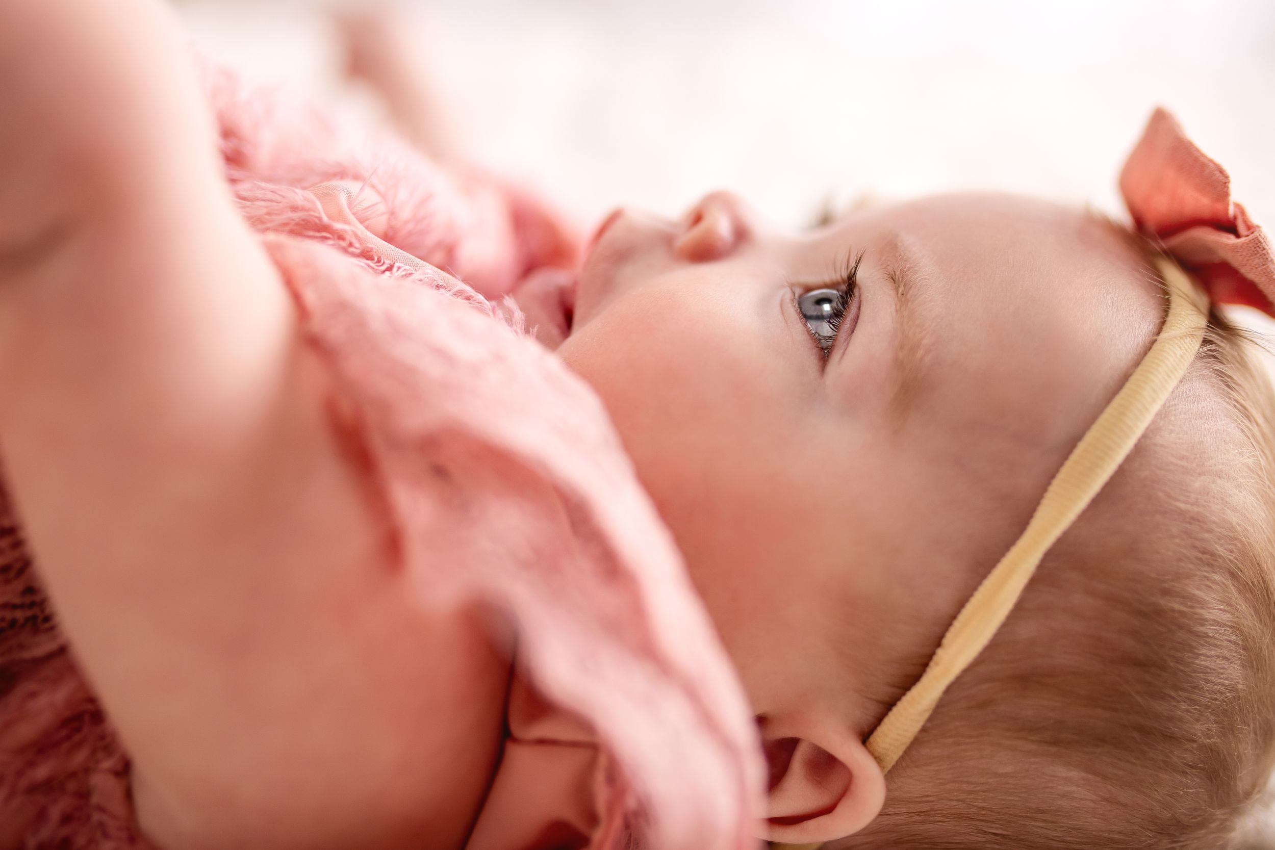 Baby girl on a bed in a studio with sparkling eyes and a pink dress