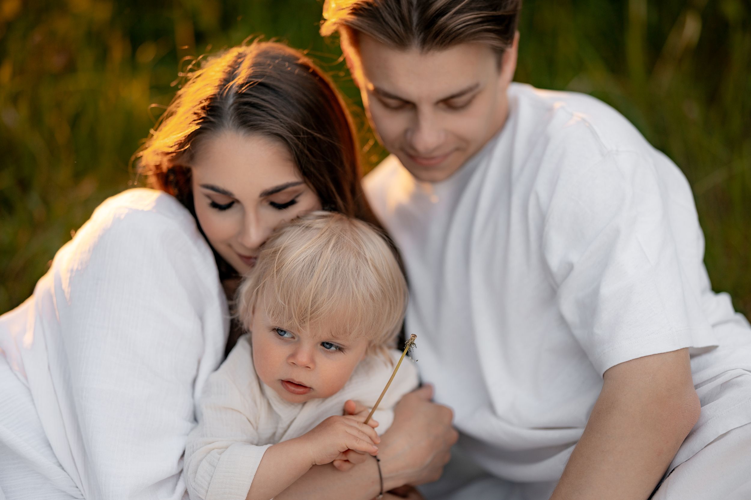 A small child nestles between parents wearing white clothing at sunset.