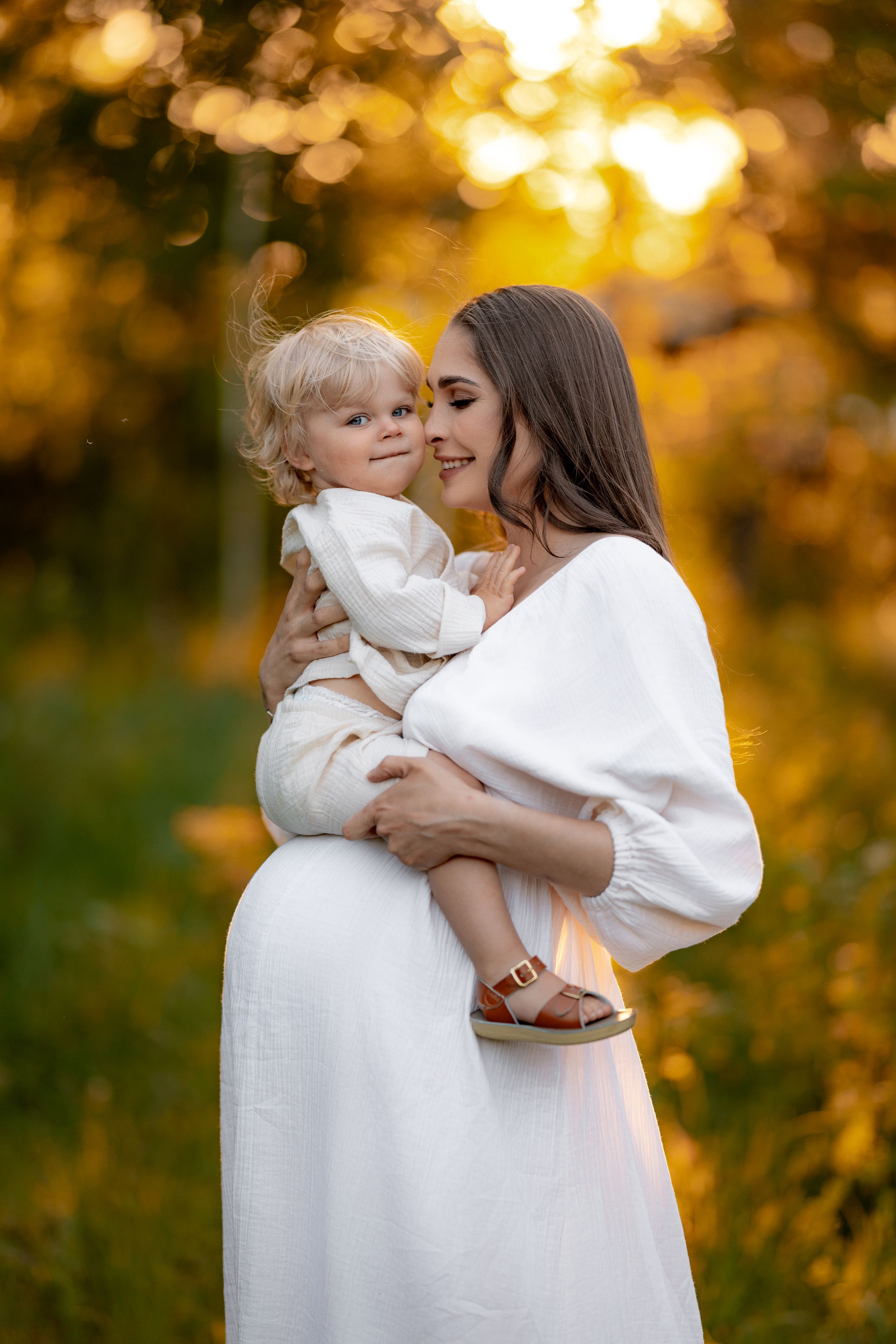 A woman in white embraces a small child against a golden sunset background.