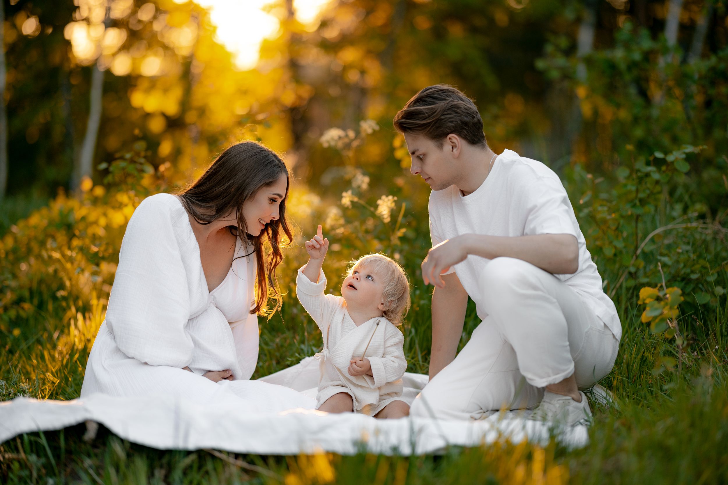 A family sits together on a white blanket in a sunlit meadow during golden hour.