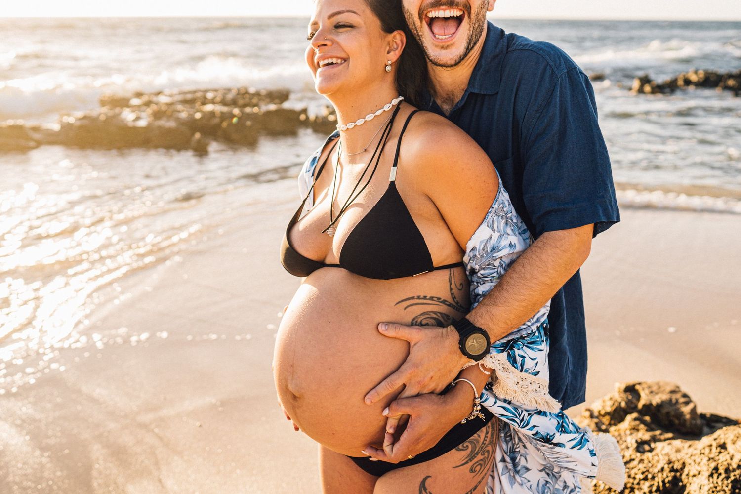 A beachside maternity photo with a couple embracing during golden hour.