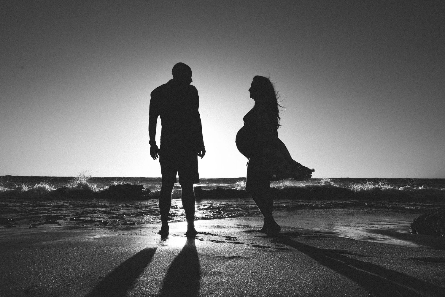 Dramatic black and white silhouette of a couple on beach at sunset.