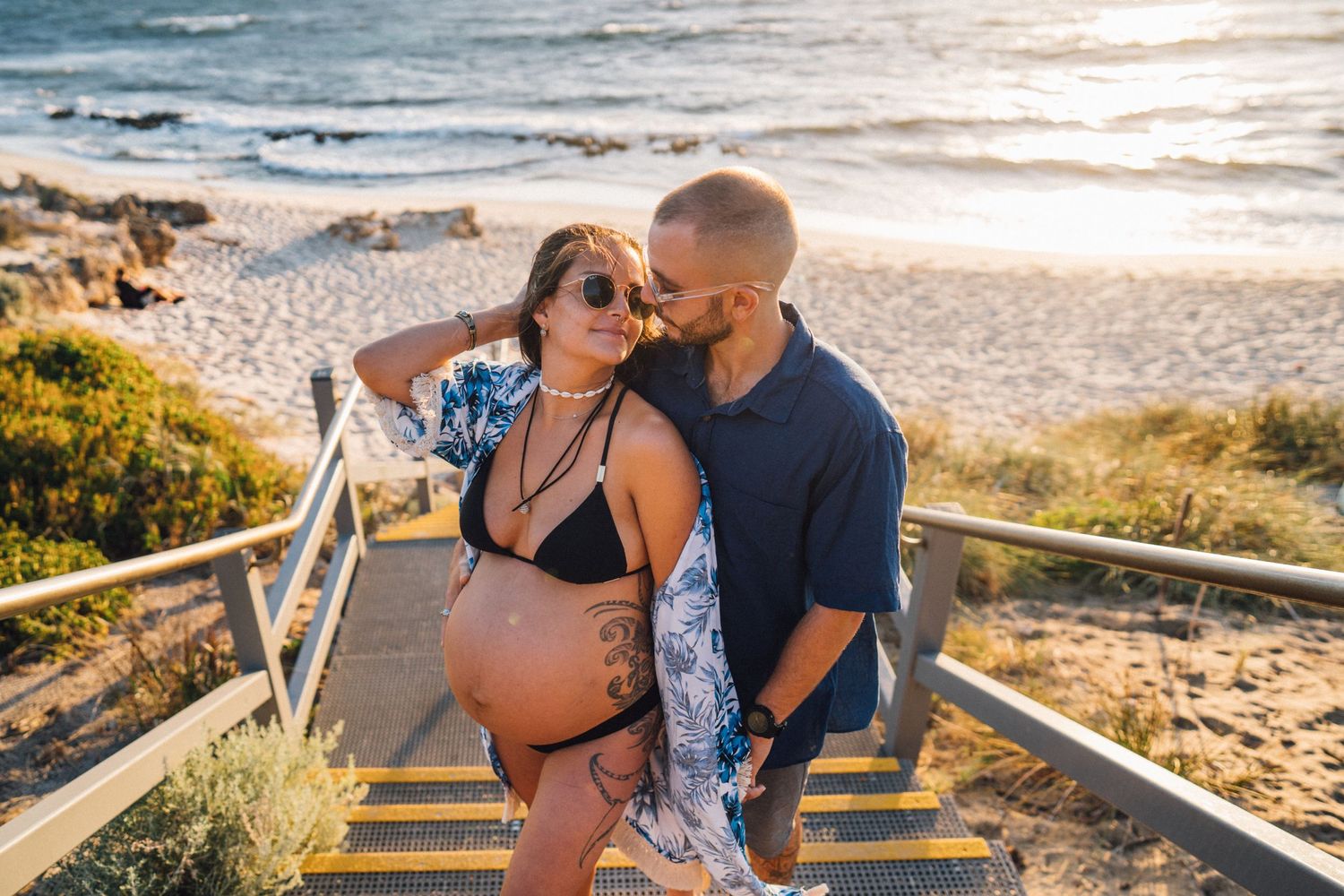 Maternity photo on coastal stairs with ocean backdrop during golden hour.