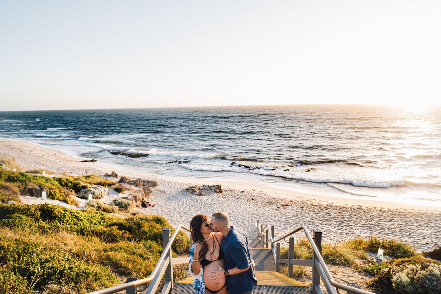 Romantic beachside photo on wooden steps with ocean view at sunset.