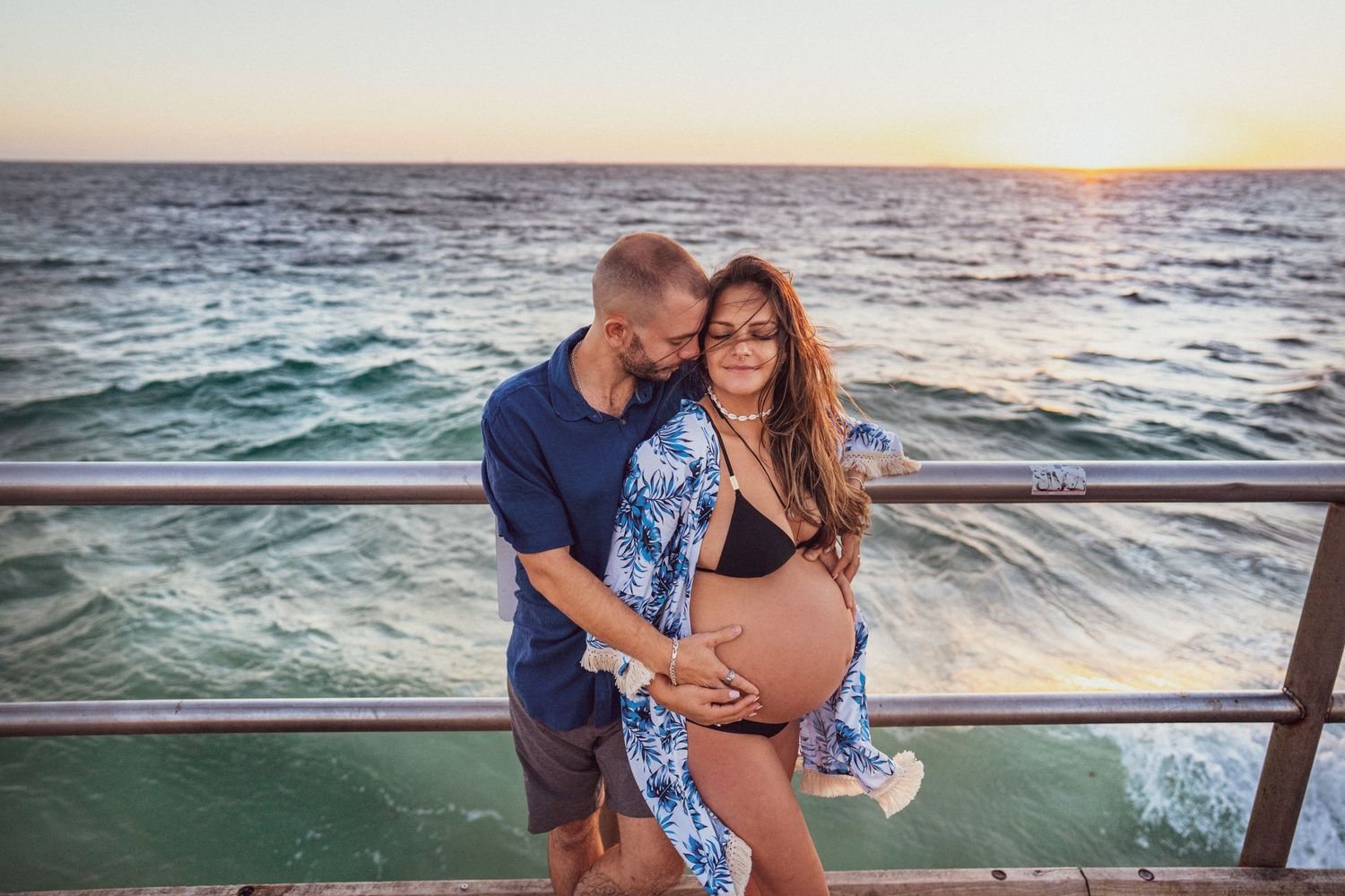 Maternity photo on an oceanside pier at sunset with mother wearing blue floral kimono.