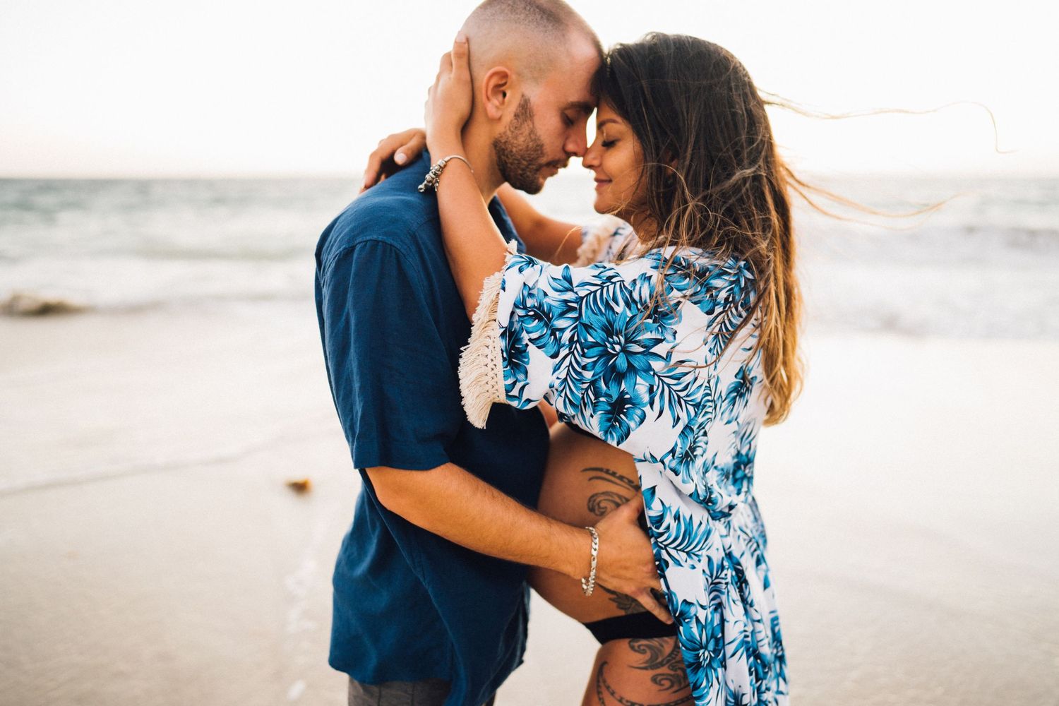Romantic beach portrait with couple in blue attire embracing at ocean's edge.
