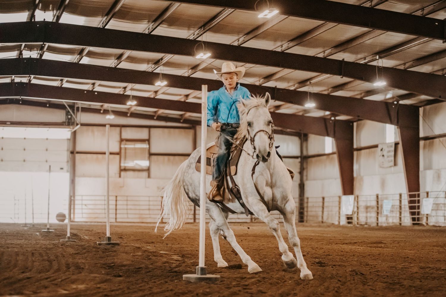 White horse and rider training in a large indoor equestrian arena.