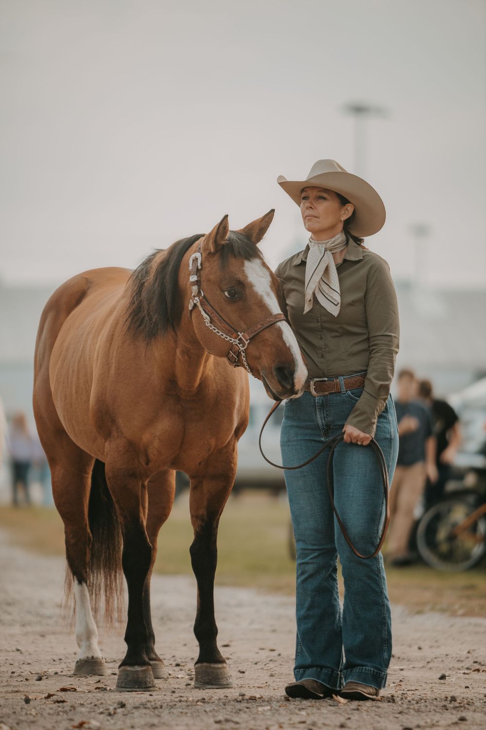 A bay horse with black mane standing with handler in western wear at equestrian event.