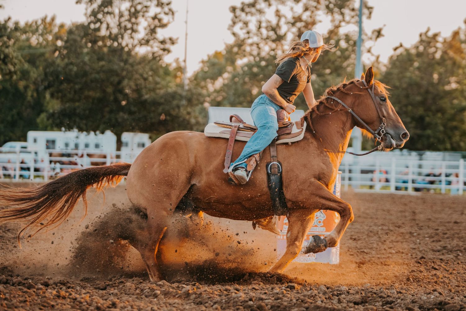 Horse and rider sprinting through dirt arena creating dramatic dust cloud during competition.