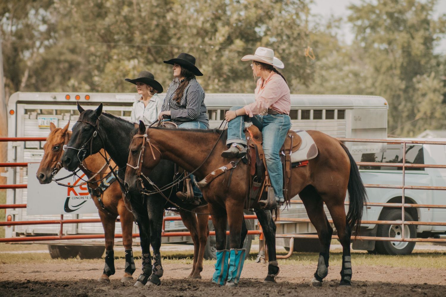 Three riders on horseback lined up along rodeo arena fence.