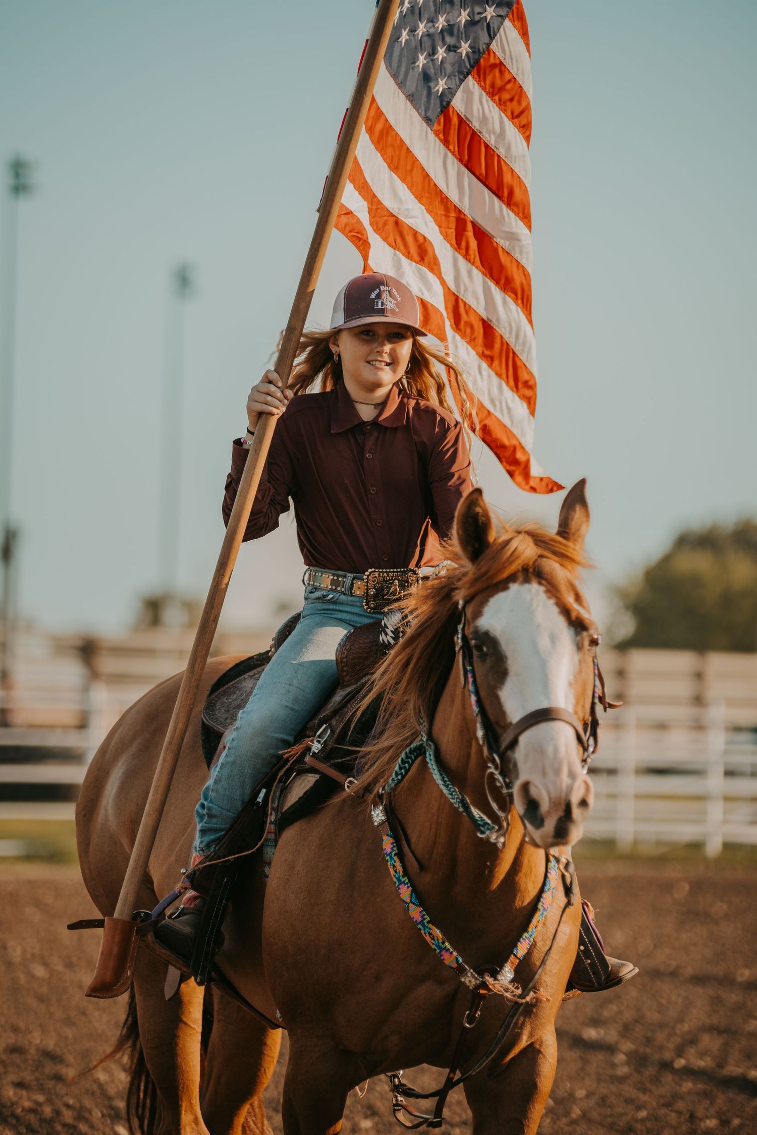 Rider carrying American flag on horseback in western rodeo arena.