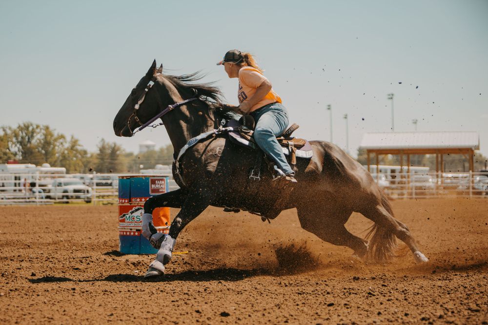 A horse and rider racing around blue barrels during a high-speed rodeo competition.