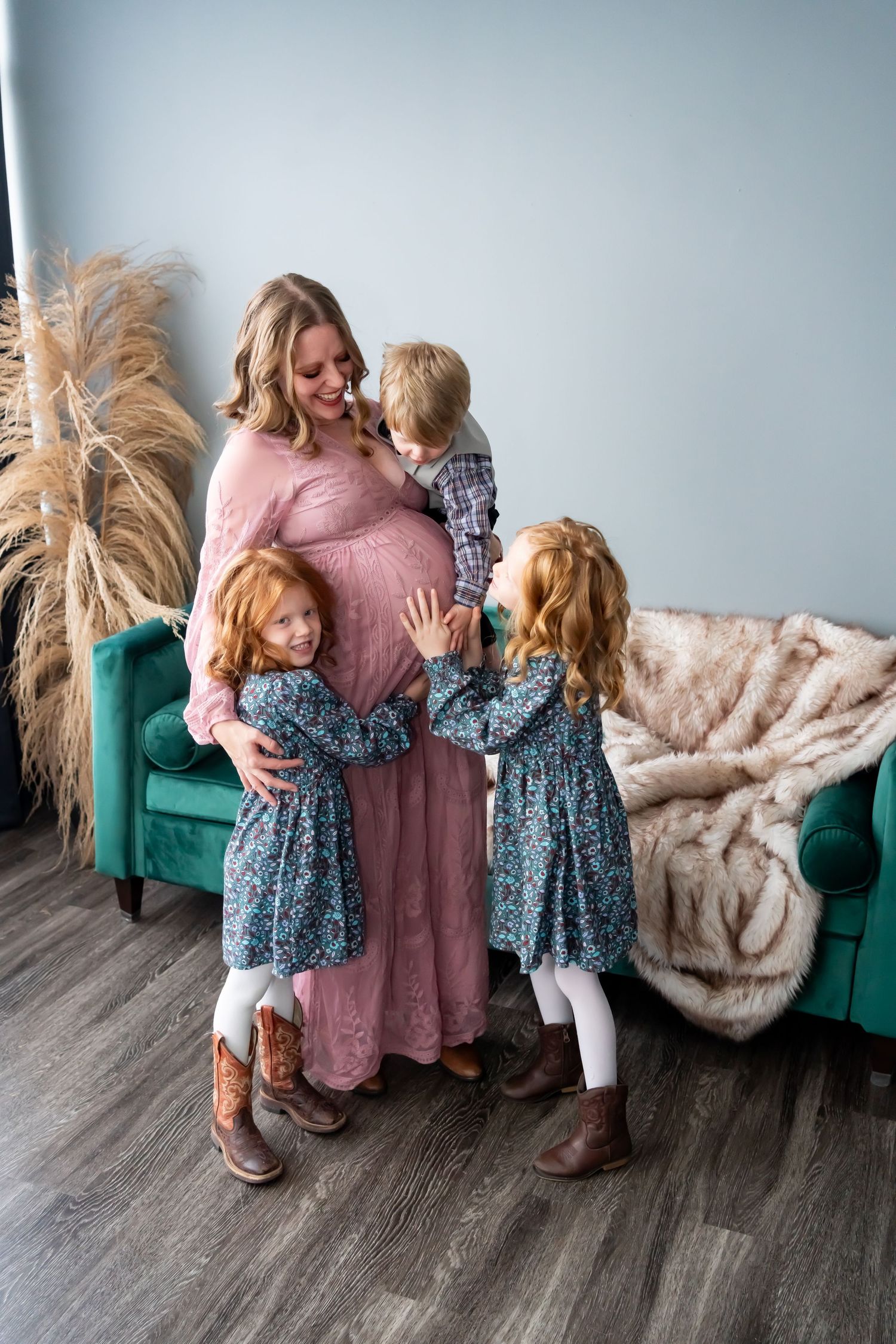 A maternity family photo with children touching mother's baby bump in a cozy indoor setting.