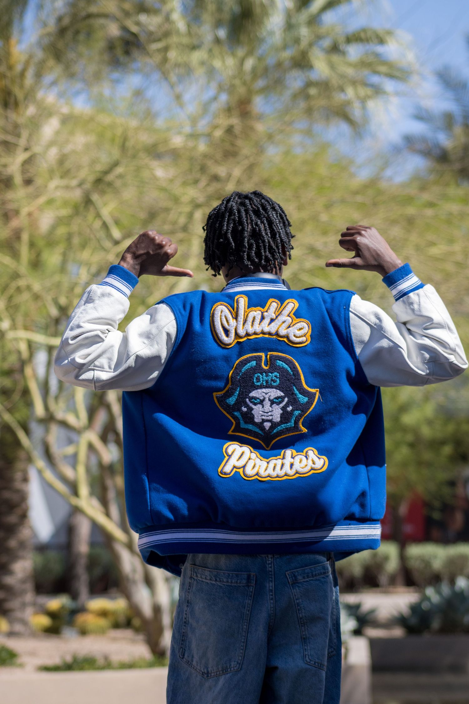 Back view of Olathe Pirates OHS varsity jacket with mascot logo displayed outdoors.