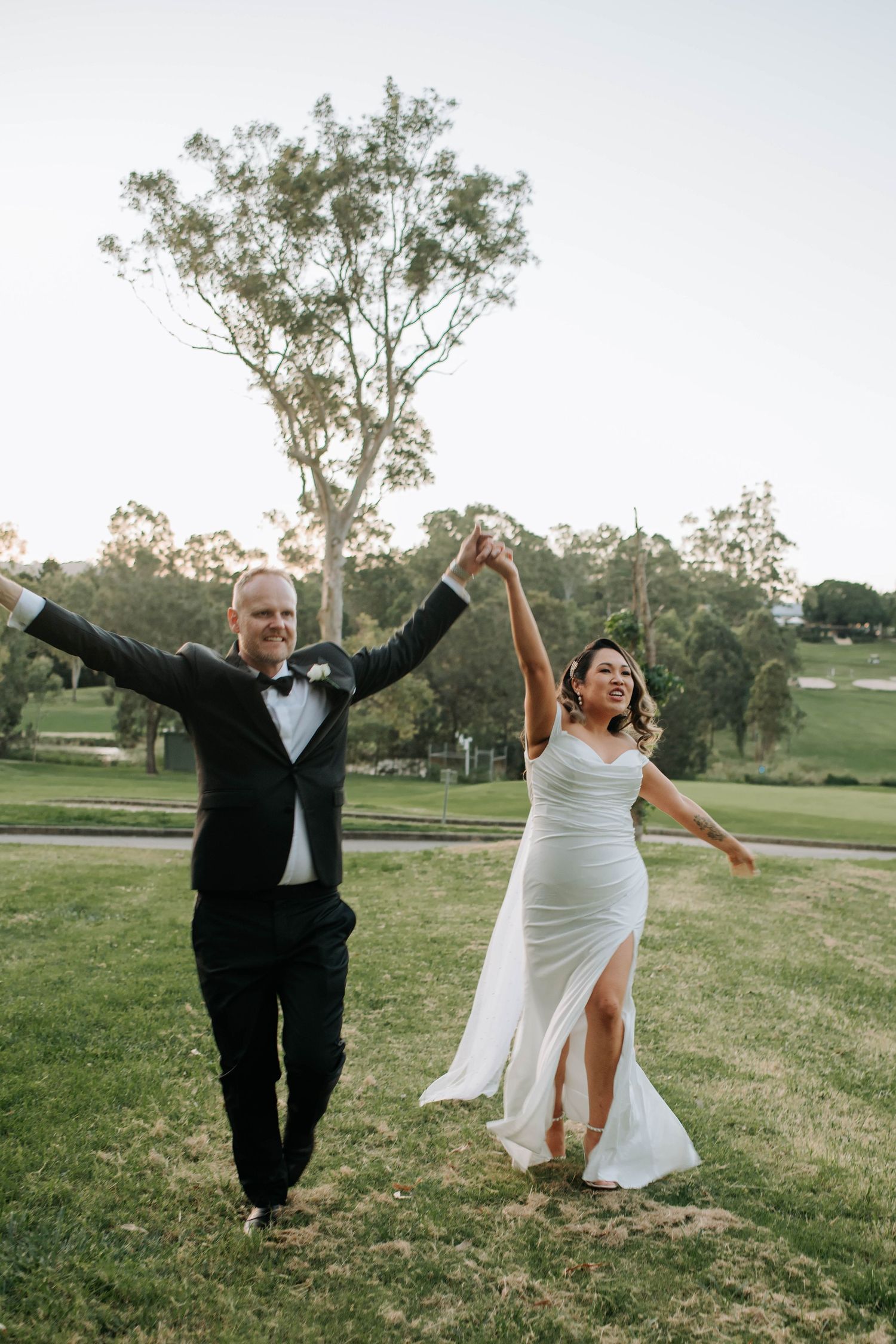Newlyweds celebrating with raised hands on grassy hill during outdoor wedding.
