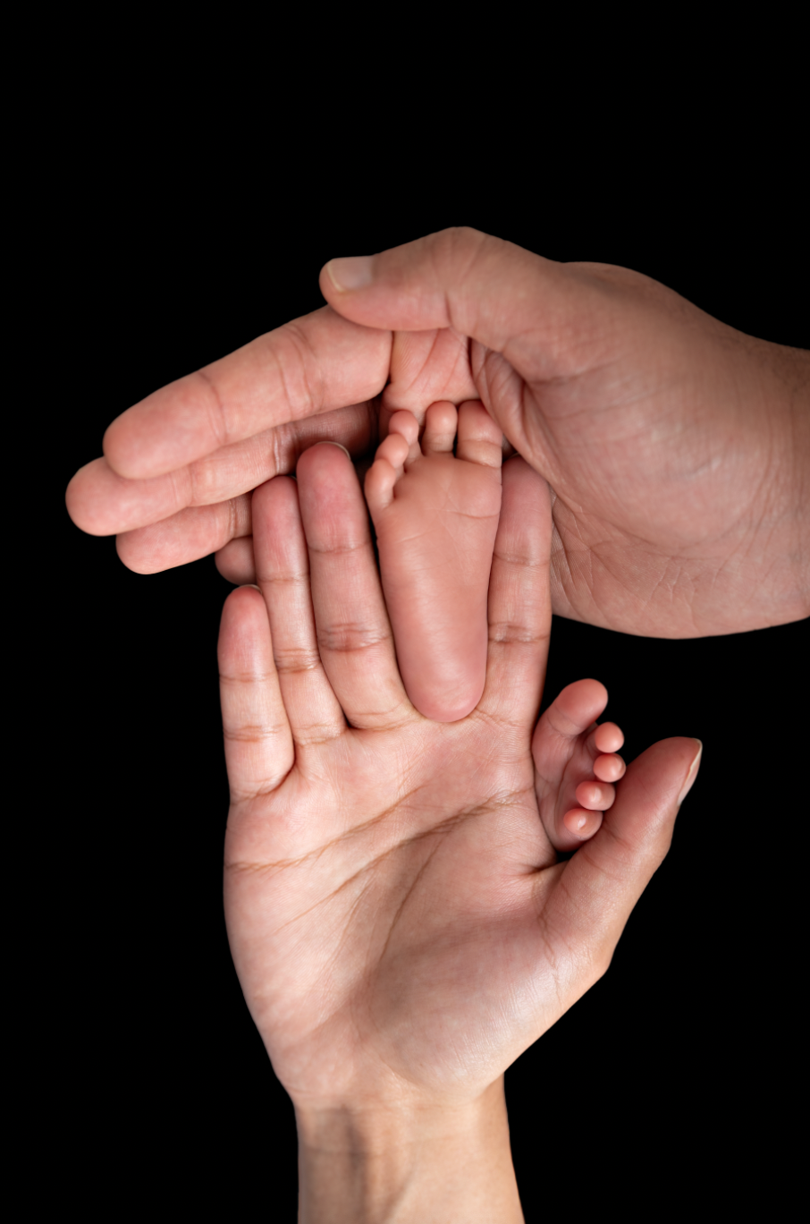Two adult hands gently cradling tiny newborn baby feet against a black background.