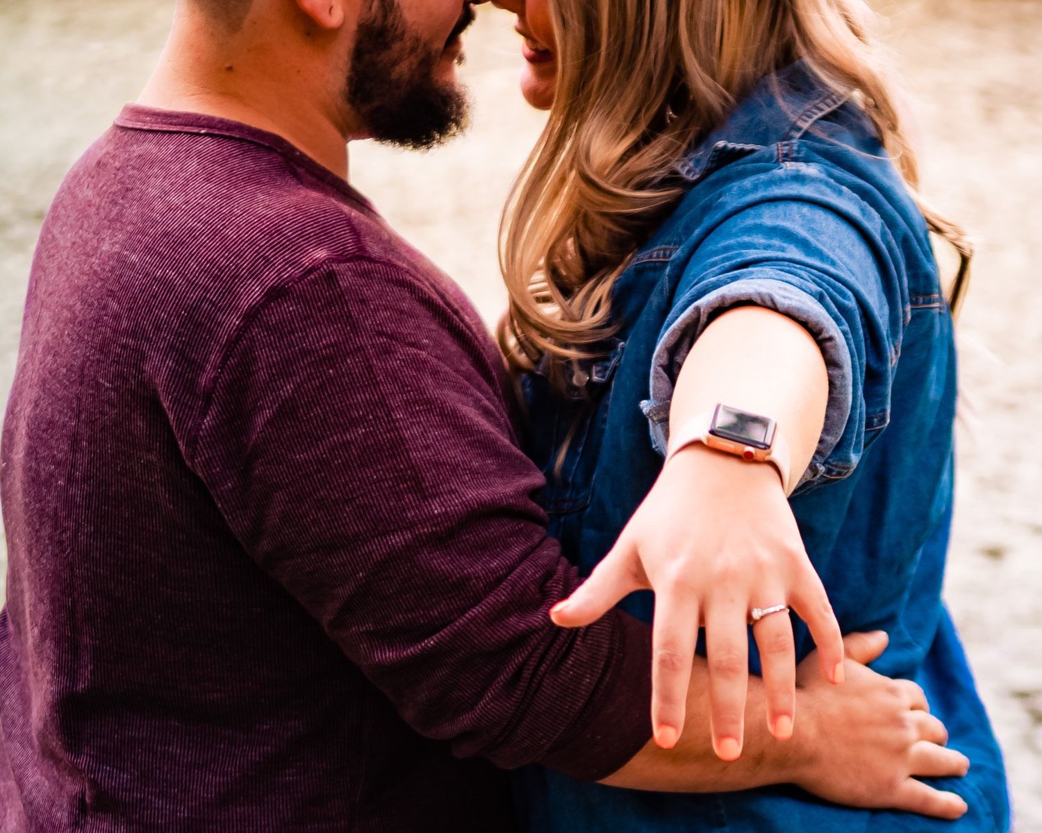 A couple embracing and showing off an engagement ring in an outdoor setting.