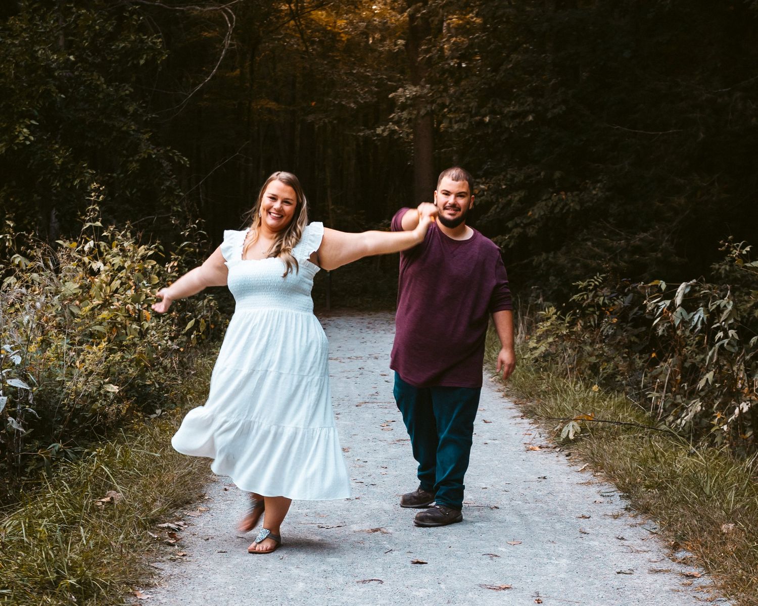 Two people dance joyfully together on a sunlit dirt path through the woods.