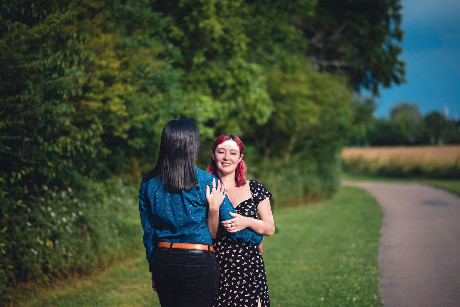 Couple walking along scenic pathway with green summer landscape in background.