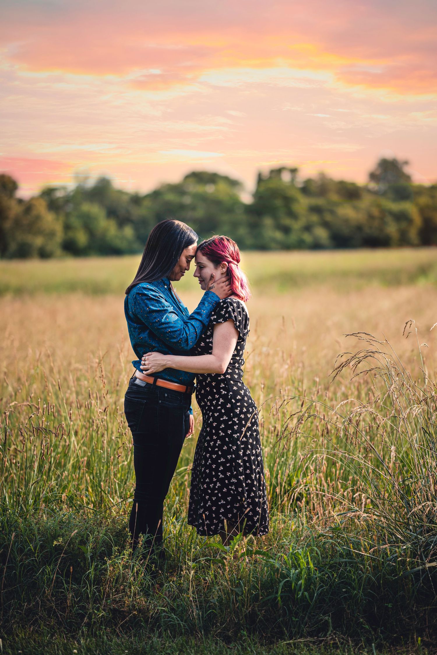 A couple shares an intimate moment in a golden field at sunset with tall grass swaying in the breeze.