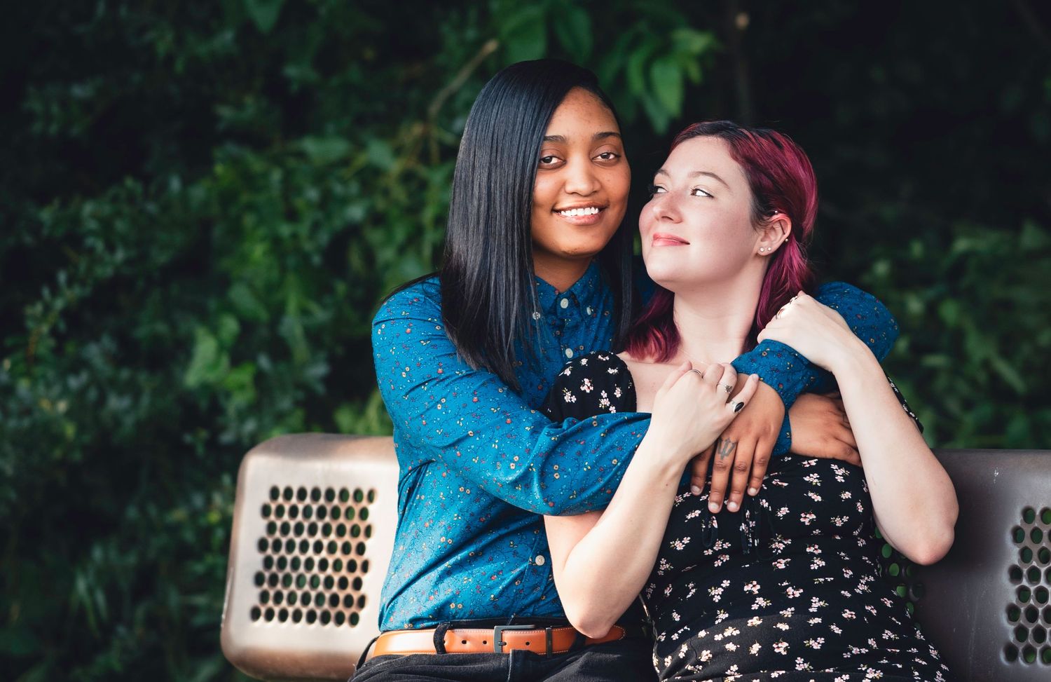 Two people share a tender moment together while sitting on a wooden bench in a park.