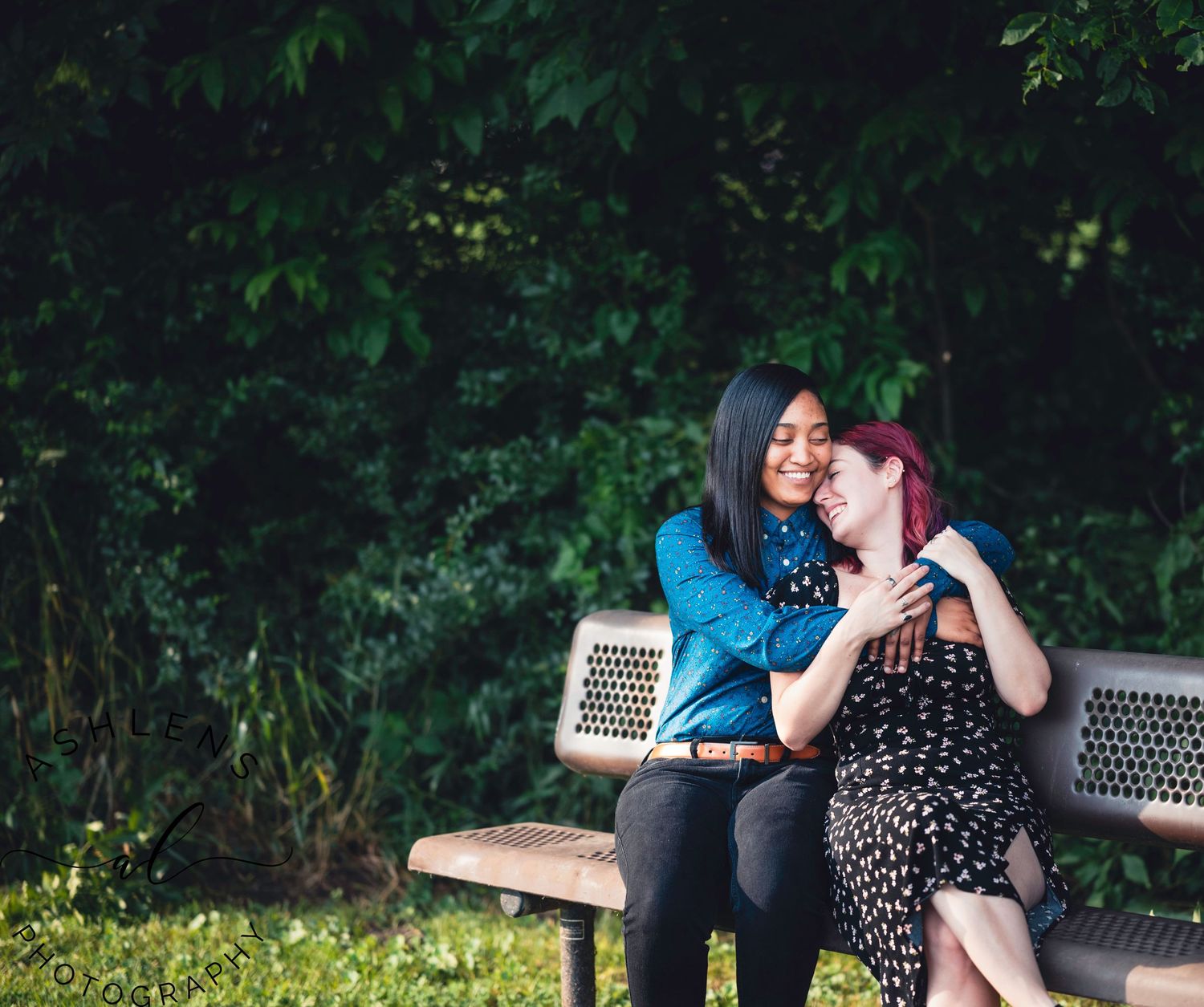 A couple shares affectionate moments on a wooden bench surrounded by lush greenery.