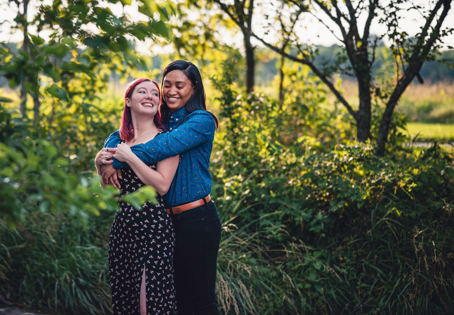 Two people embrace in a natural outdoor setting with sunlit trees in the background.