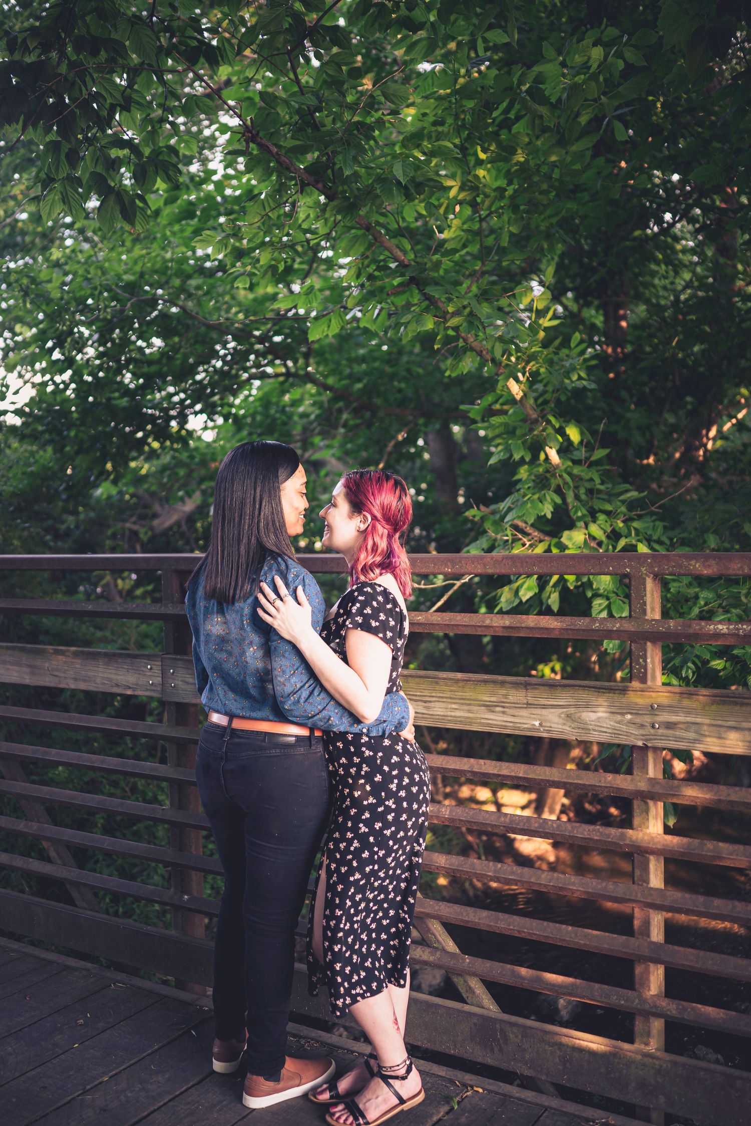 Couple sharing romantic moment on wooden bridge surrounded by lush green foliage.