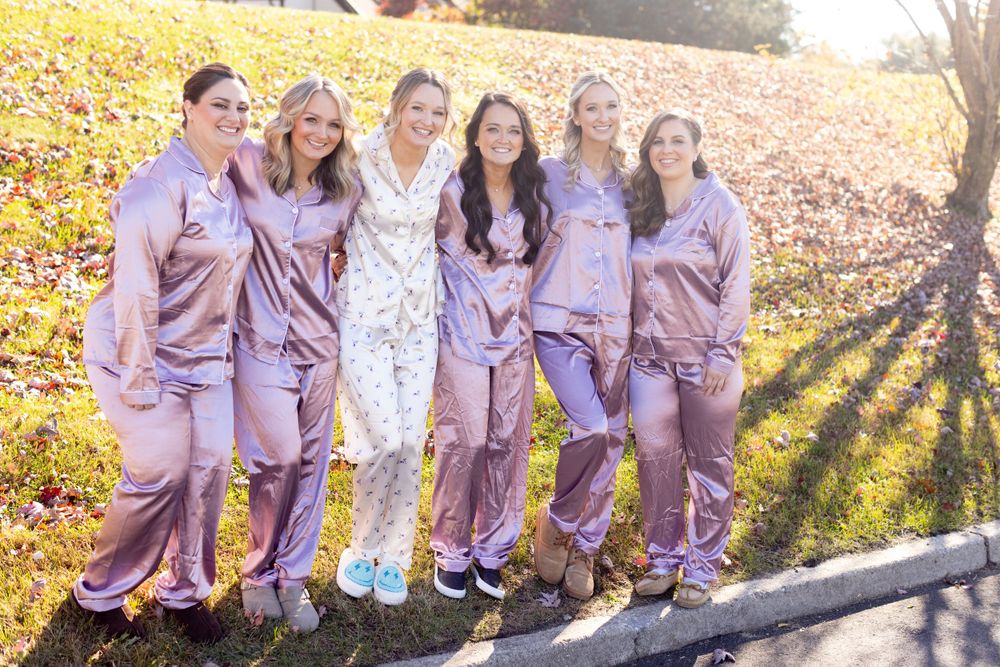 Bride and five bridesmaids pose outdoors in matching lavender satin pajama sets on wedding day.