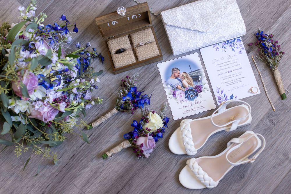 Wedding flat lay featuring wildflower bouquet, rings, invitation, boutonnieres, and white sandals.