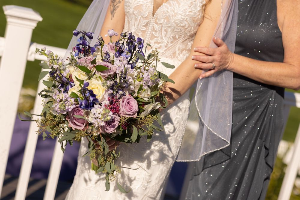 Close-up of bride in lace wedding dress holding purple and lavender floral bouquet with elegant veil.
