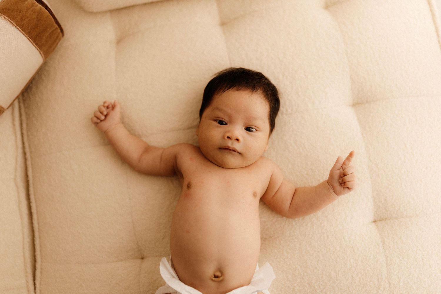 Baby lying on cream colored tufted couch wearing diaper.
