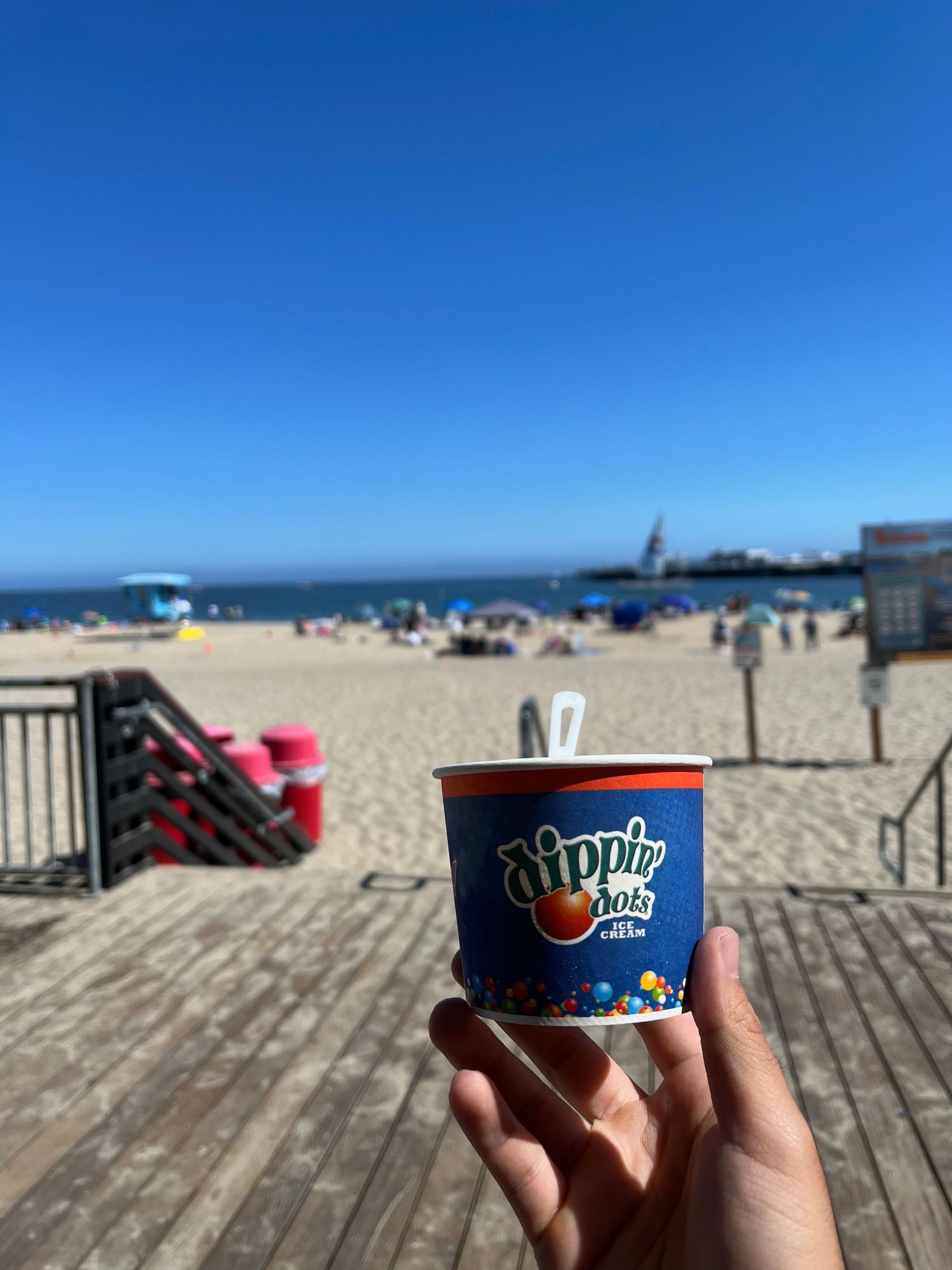 A small ice cream cup held up on a wooden boardwalk at the beach.