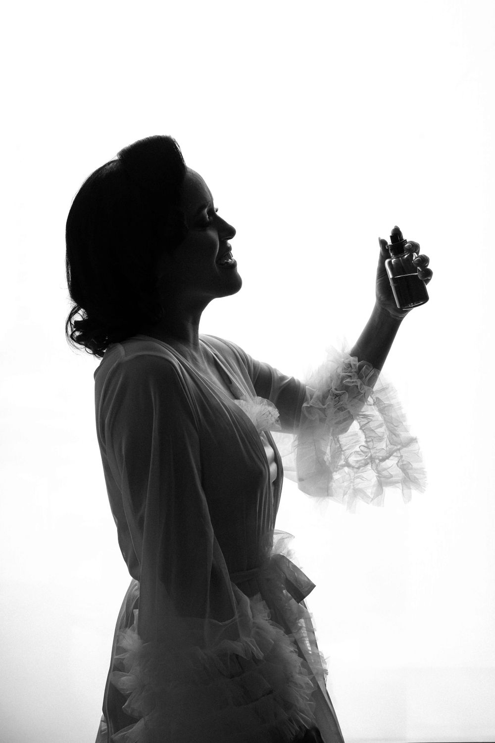 Silhouette of a bride in a lace dress against a bright background, captured in black and white.