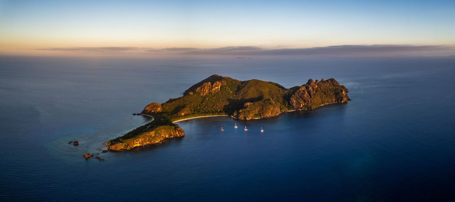 Aerial view of mountainous island surrounded by calm ocean waters at sunset.