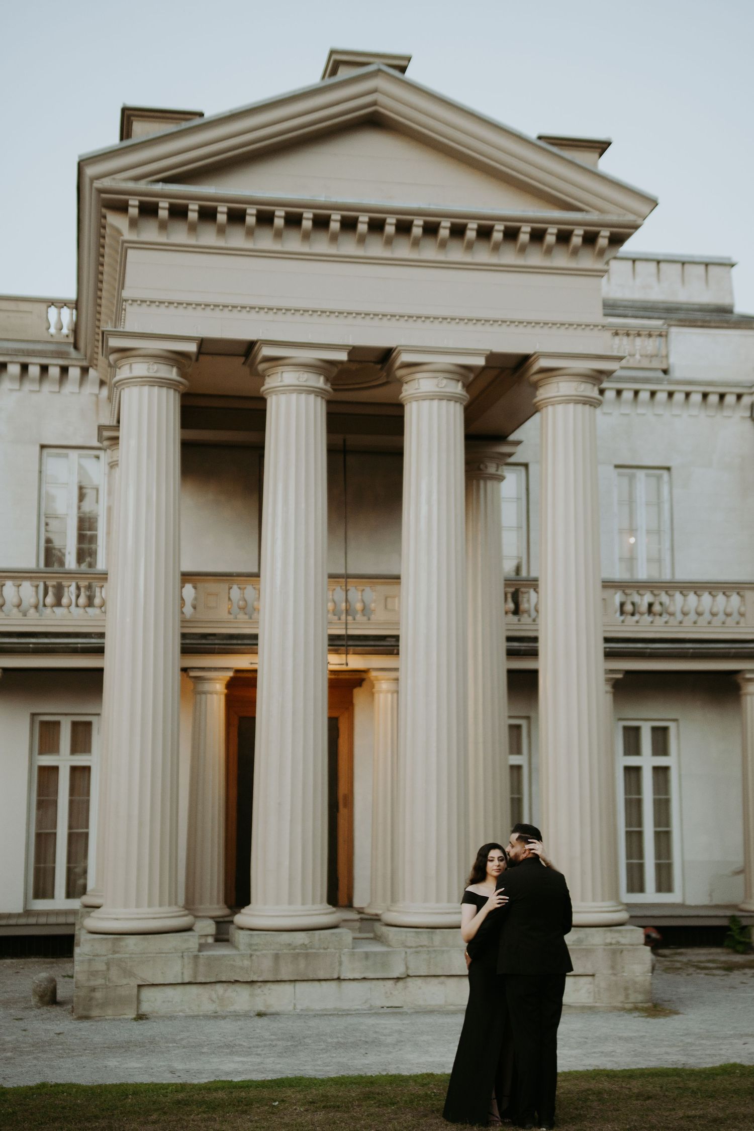 Couple embracing in front of neoclassical building with grand white columns at dusk.
