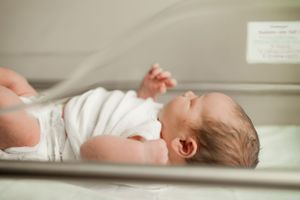 Close-up of a newborn baby in white clothing lying peacefully in a hospital bassinet.