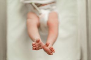 Close-up of tiny newborn baby feet and legs resting on a soft white blanket in a hospital.